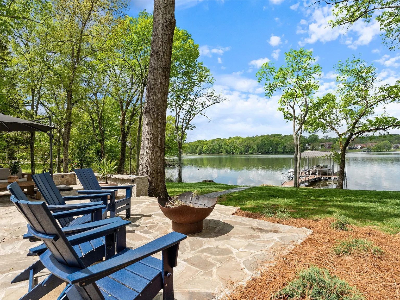 Lakeside patio with blue chairs, mature trees, and a dock in Middle Tennessee